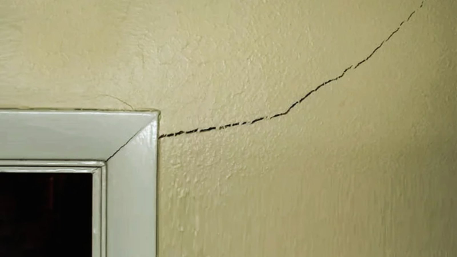 A visible crack in the wall of a room, adjacent to a closed door, indicating potential structural issues.