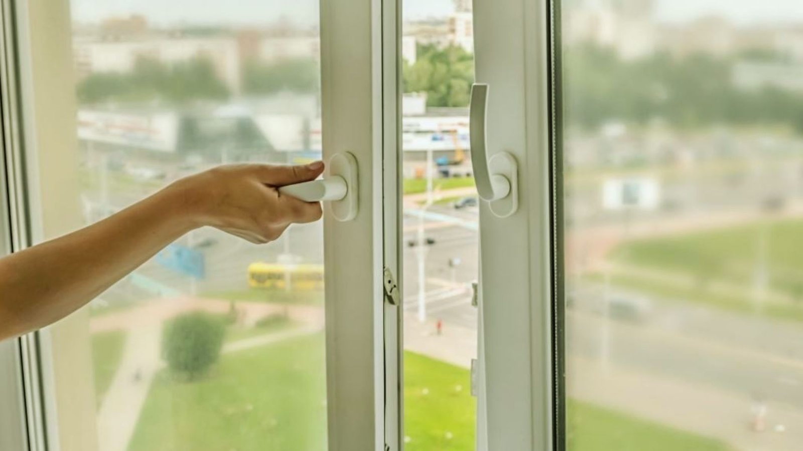 A person is opening a window by grasping a white handle.