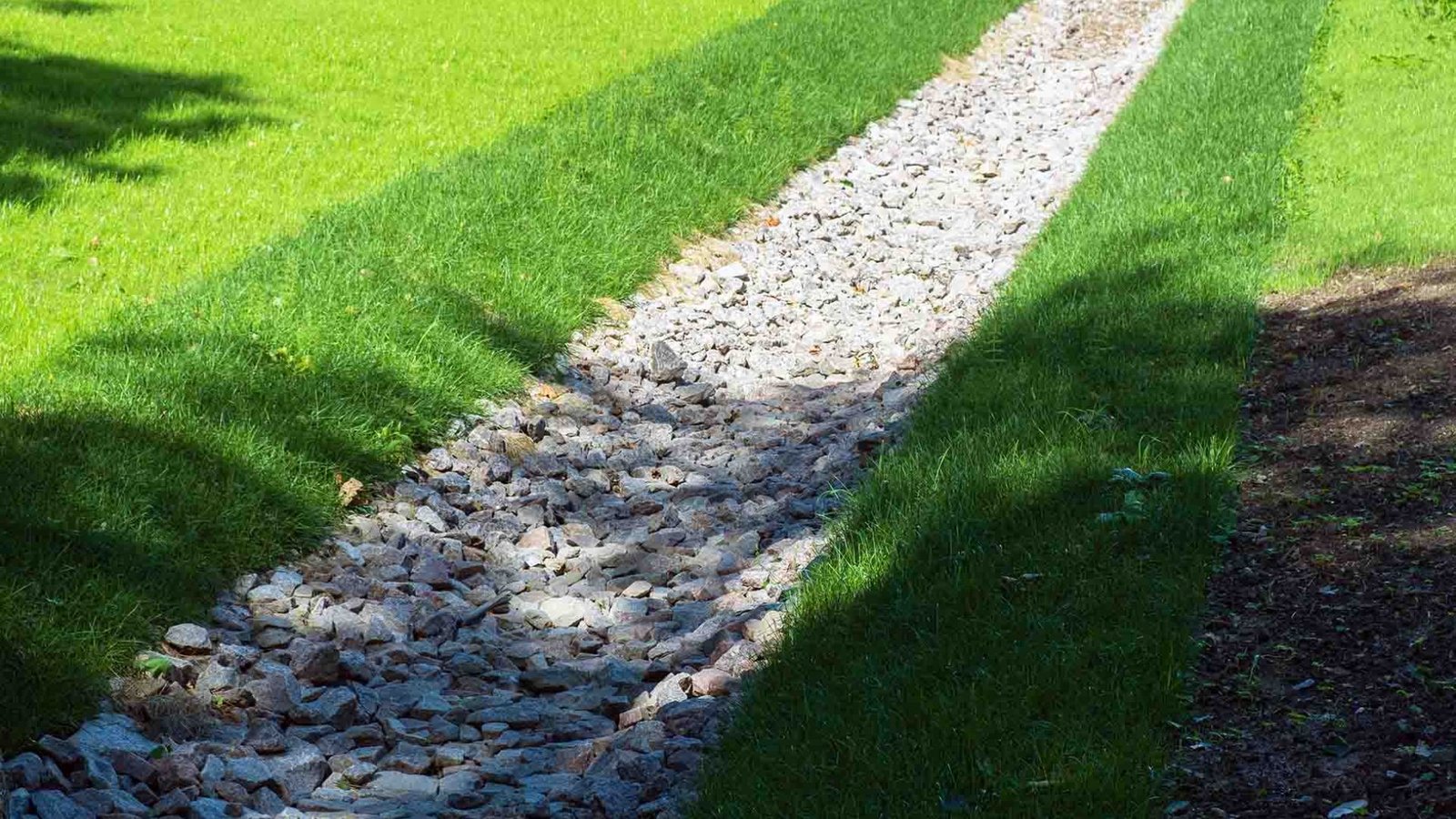 A long gravel path stretches through a lush grassy field under a clear blue sky.
