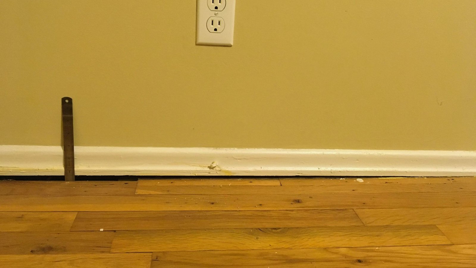 A close-up of a wooden floor featuring a hole in the wall, exposing the space beyond.