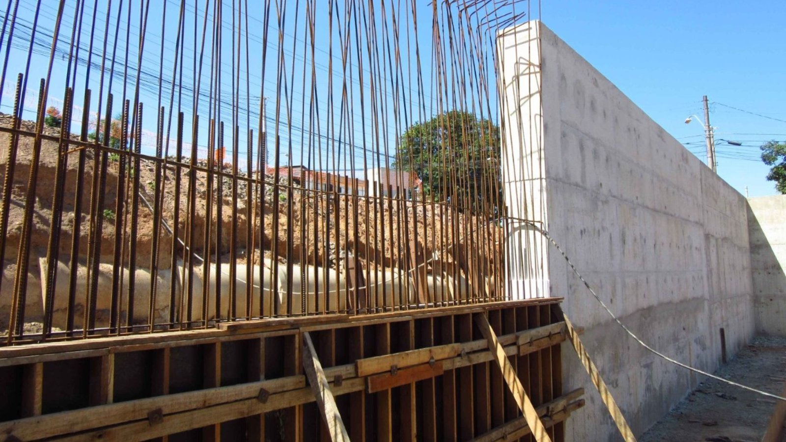 A construction worker builds a concrete wall at a construction site, with tools and materials visible around them.