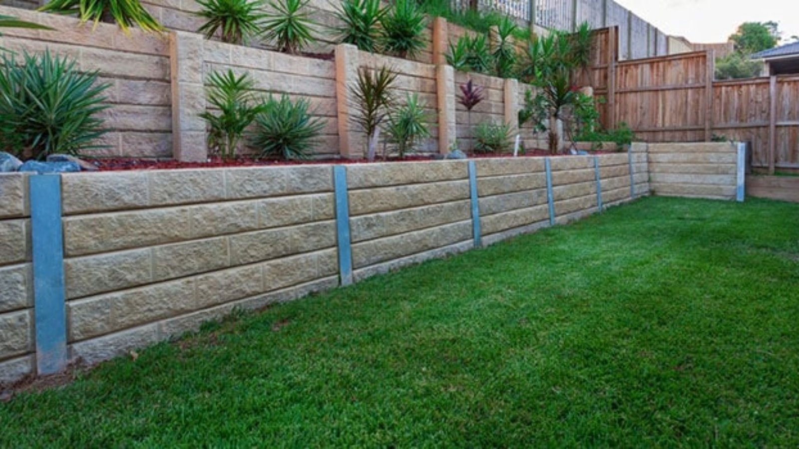 A backyard featuring a stone retaining wall surrounded by lush grass and various plants.