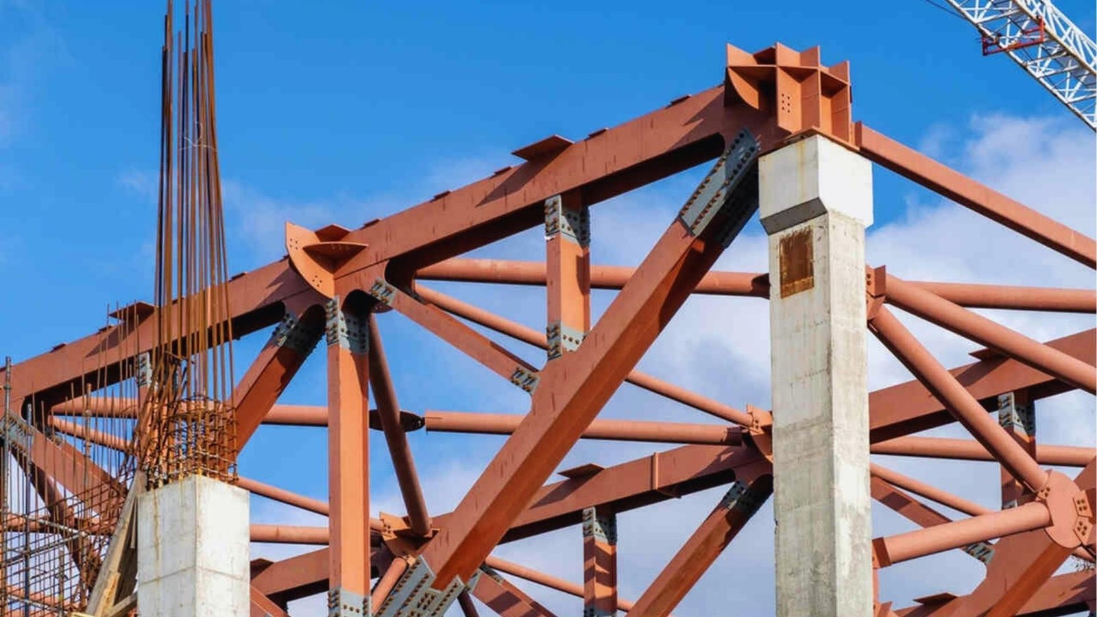  A large steel structure is under construction, showcasing beams and scaffolding against a clear blue sky.