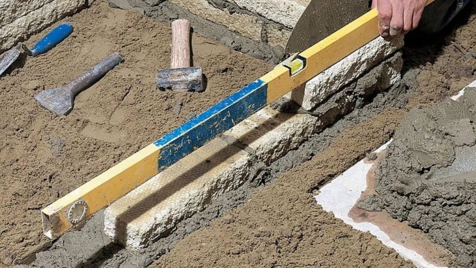 A person measures a brick's size using a wooden ruler, focusing intently on the measurement process.