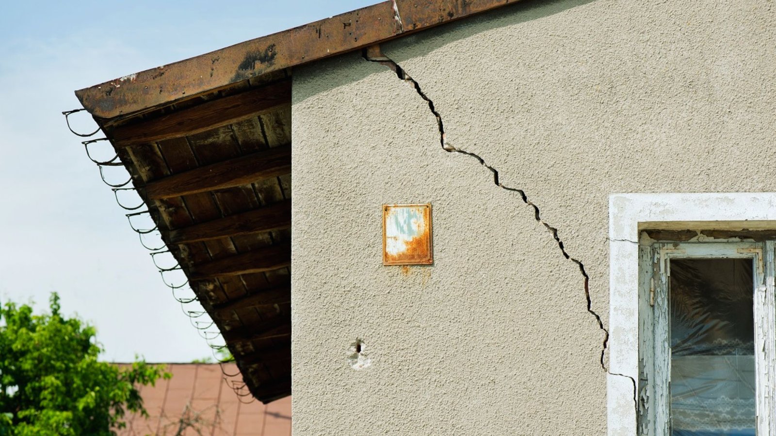 A crack in the side of a house with a warning sign attached, indicating potential structural issues.