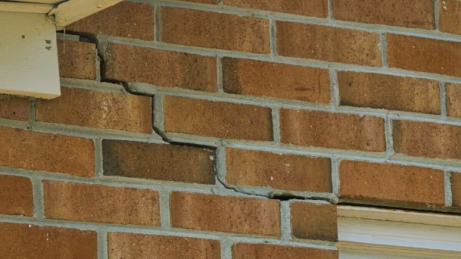 A close-up view of a crack in the brick wall of a house, revealing the structural damage and wear over time.