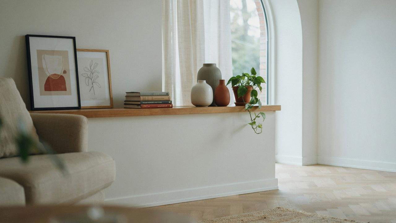 Half wall room divider with a wide display shelf decorated with books, plants, and framed artwork.